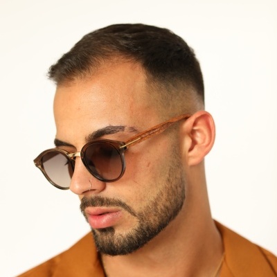 Óculos de sol com armação castanha translúcida e lentes escuras, homem com camiseta castanha e barba