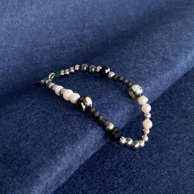 Pulseira com contas variadas em preto, branco e prata sobre fundo azul