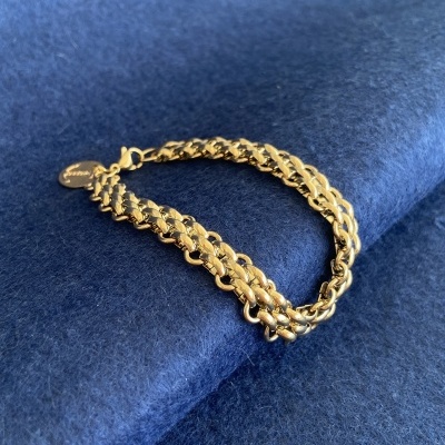 Pulseira dourada de elos trançados sobre tecido azul escuro