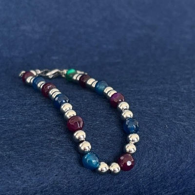 Pulseira azul, verde e borgonha com esferas prateadas sobre tecido azul escuro