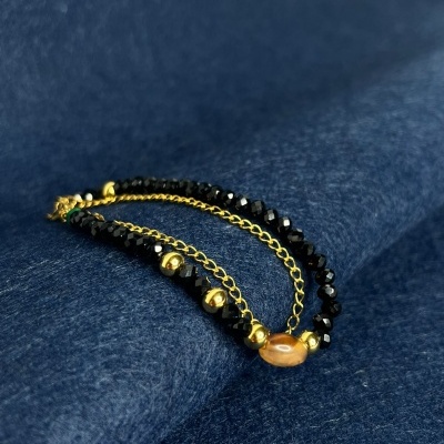 Pulseira com contas pretas e douradas sobre tecido azul escuro