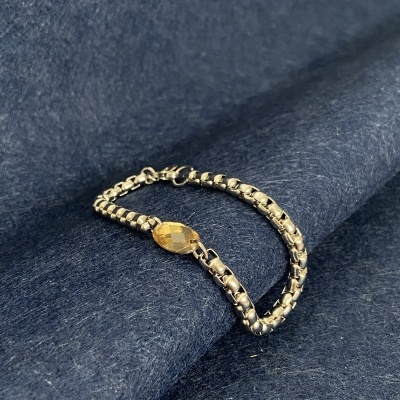 Pulseira dourada com fecho oval sobre tecido azul escuro