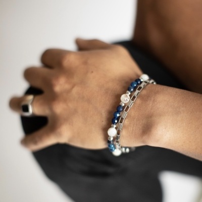 Braço com pulseiras azul, branco e prata e anel prateado em fundo branco e preto
