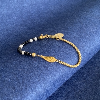 Pulseira dourada com contas pretas e brancas sobre tecido azul.