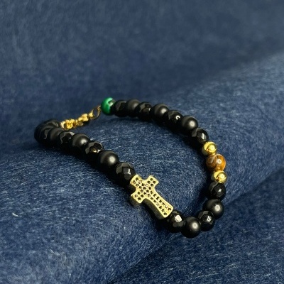 Pulseira preta com cruz dourada e contas amarelas e verdes sobre tecido azul escuro