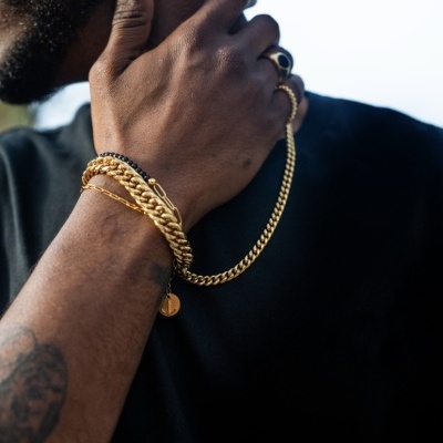 Pulseira dourada de correntes no pulso esquerdo com anel dourado e tatuagem no antebraço