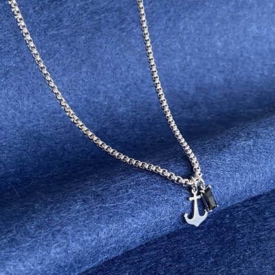 Colar prateado com pendentes de âncora e pedra preta sobre tecido azul