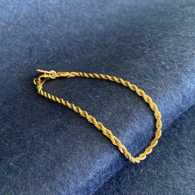Pulseira dourada torcida sobre tecido azul
