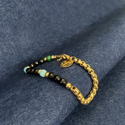 Bracelete com contas douradas, pretas, turquesa e verdes em fundo de tecido azul escuro