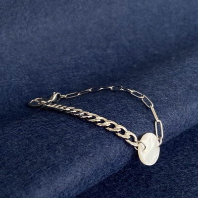 Pulseira prateada com duas correntes e pendente redondo sobre tecido azul escuro