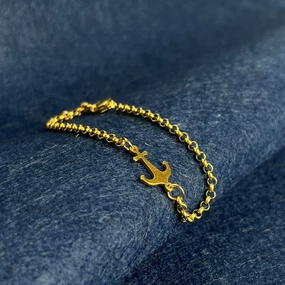 Pulseira dourada com âncora sobre tecido azul
