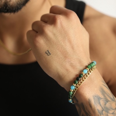 Pulseira masculina com contas verdes, azuis e corrente dourada no pulso tatuado de homem