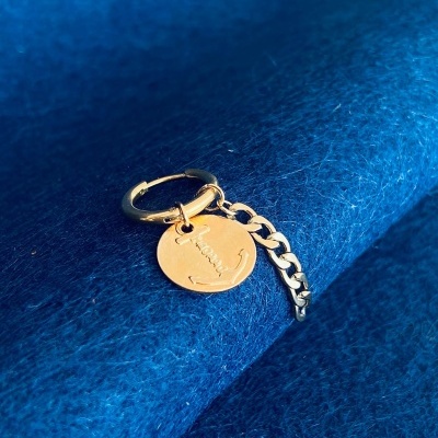 Brinco dourado com pendente circular e corrente sobre tecido azul
