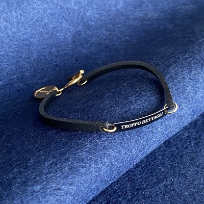 Pulseira preta com placa escrita TROPPO DETTAGLI sobre tecido azul