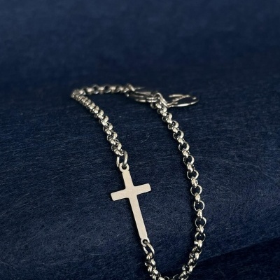 Pulseira de metal prateado com cruz em fundo azul escuro