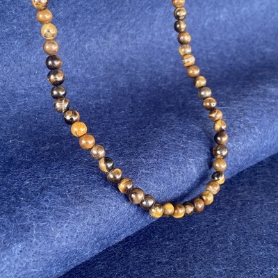 Colar com contas castanhas e amarelas sobre tecido azul escuro