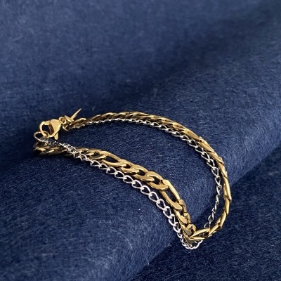 Pulseira de três correntes em metal dourado e prateado sobre tecido azul