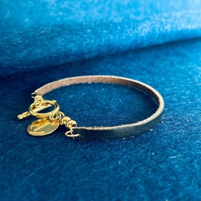 Pulseira de couro castanho com fecho dourado e pendentes numa superfície azul