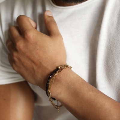 Pulseira de corrente dourada com fio preto de contas em pulso masculino com t-shirt branca