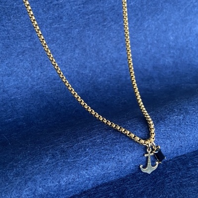 Colar dourado com pendente em forma de âncora e detalhe azul