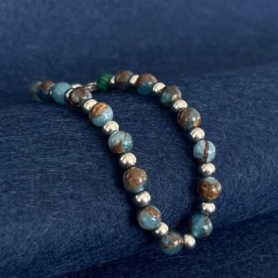 Pulseira com contas azuis e castanhas e esferas prateadas sobre tecido azul escuro