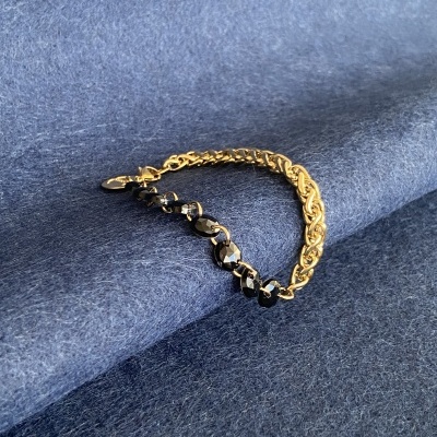 Pulseira dourada com pedras pretas sobre tecido azul.