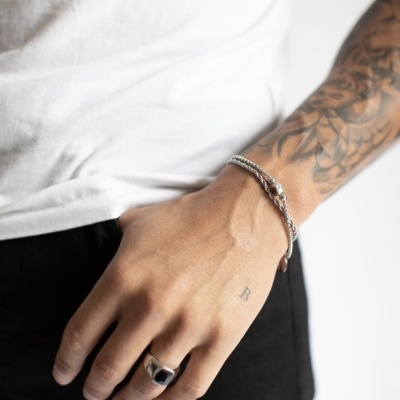 Braço masculino com pulseira prateada e anel preto