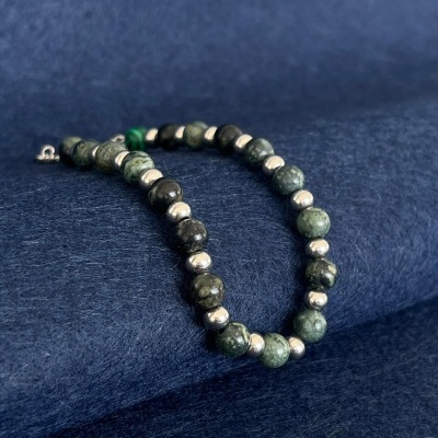 Colar de contas verdes e pretas com contas metálicas prateadas sobre fundo azul