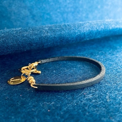 Pulseira preta com fecho e pendente dourados sobre tecido azul felpudo