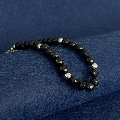 Colar preto com contas facetadas e esferas prateadas sobre tecido azul