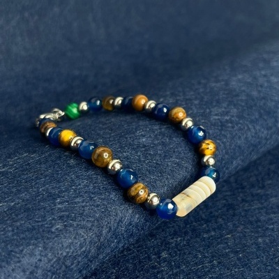 Pulseira com contas azuis, castanhas, prateadas e brancas sobre tecido azul.