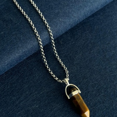 Colar com pendente de pedra castanha e corrente prateada em fundo azul escuro