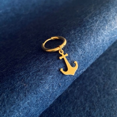 Brinco dourado com pendente de âncora sobre tecido azul