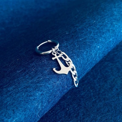 Argola prateada com pendente de âncora e corrente sobre tecido azul