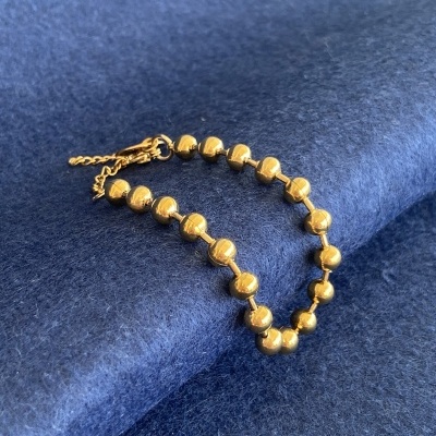 Pulseira dourada com bolas sobre tecido azul.