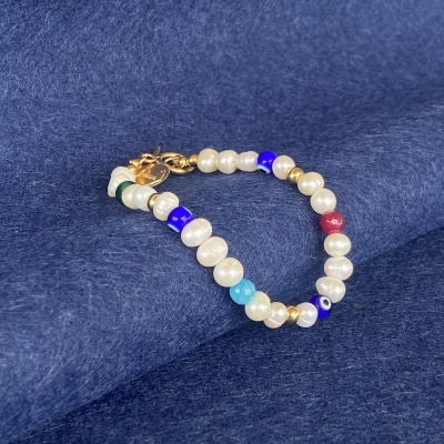 Pulseira de pérolas e contas coloridas sobre tecido azul.