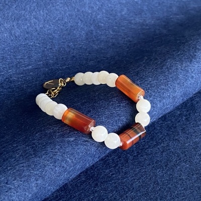 Pulseira com contas brancas e alaranjadas sobre tecido azul.