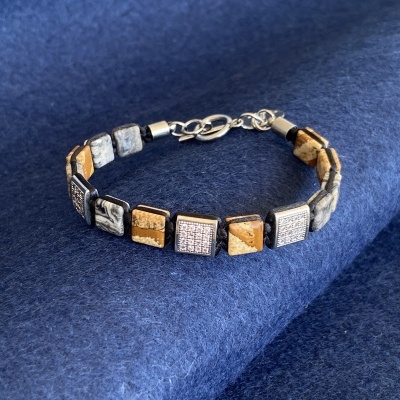 Pulseira com contas quadradas em pedra e cristais com fecho metálico prateado sobre têxtil azul.