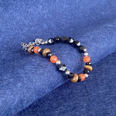 Pulseira de contas pretas facetadas, laranjas, de madeira e prateadas sobre tecido azul.