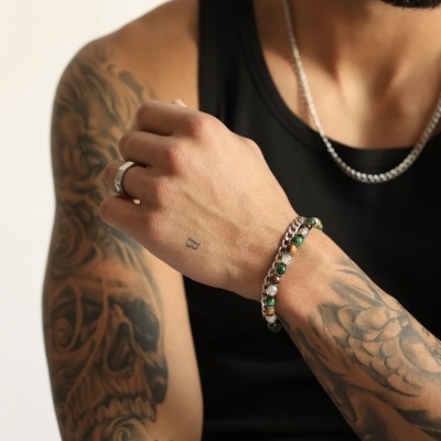 Braço tatuado com pulseira colorida, anel e corrente prateada