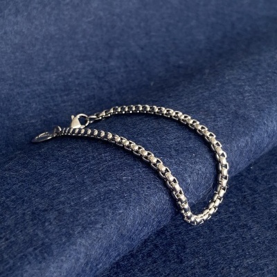 Pulseira prateada com elos quadrados sobre tecido azul escuro aveludado