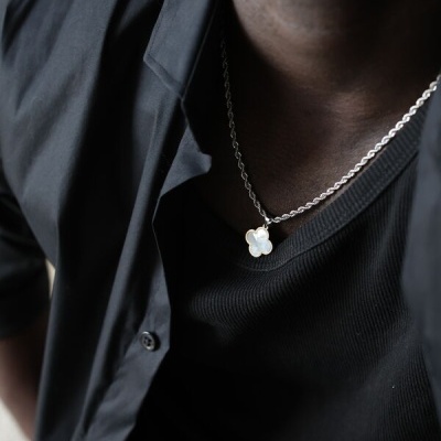 Colar prateado com pendente de flor usado por pessoa com camisa preta