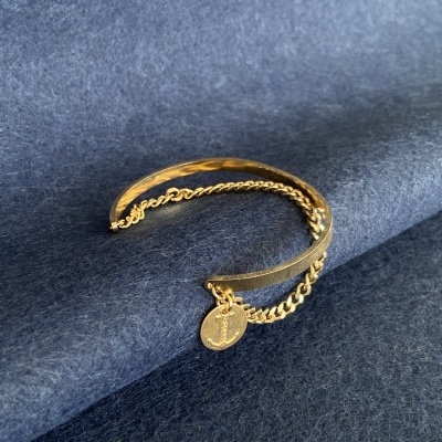 Pulseira dourada em metal com corrente e medalha, sobre tecido azul.