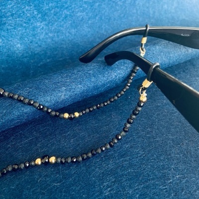 Cordão para óculos com contas pretas e douradas preso em armação preta