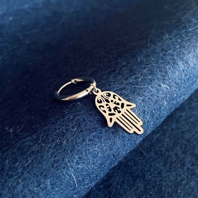Brinco de argola prateado com pendente de mão Hamsa sobre tecido azul escuro