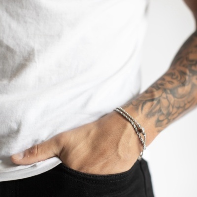Pulso masculino com pulseira prateada, tatuagens e roupa casual branca e preta