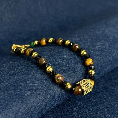 Pulseira de contas castanhas, pretas e douradas sobre tecido azul escuro