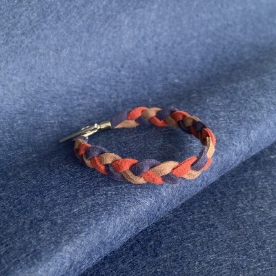 Pulseira trançada em tecido colorido com fecho metálico sobre tecido azul