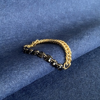 Pulseira masculina com elos dourados e pretos sobre tecido azul.