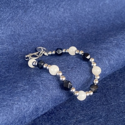 Pulseira de contas prateadas, pretas e brancas sobre tecido azul.